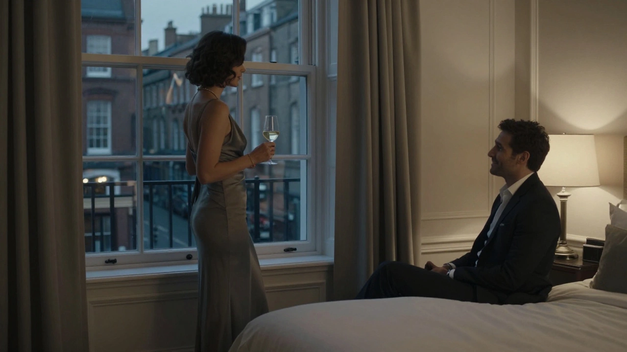 A woman in elegant dress stands by a hotel window, reflecting city lights as she talks to a man on the bed.