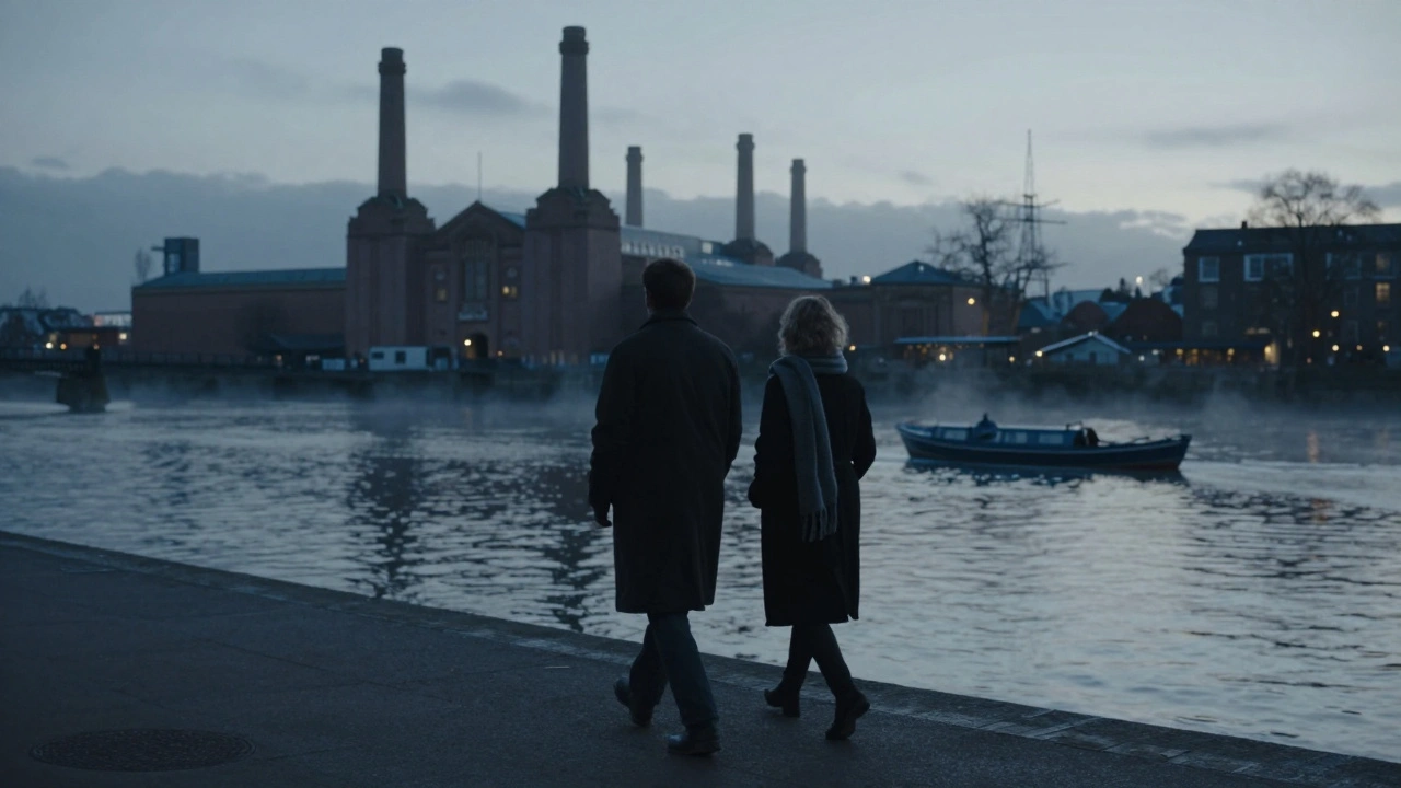 Two figures walk quietly along the Thames at dusk, the Royal Arsenal in the distance, mist rising from the water.